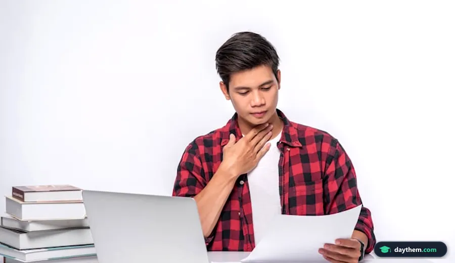 Nam sinh viên ngồi làm việc với máy tính xách tay và tài liệu giấy trên bàn