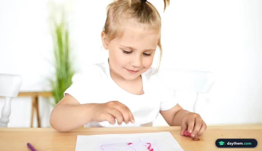 Bé gái mầm non buộc tóc đuôi ngựa ngồi tại bàn học đang tập tô màu với vẻ mặt vui tươi